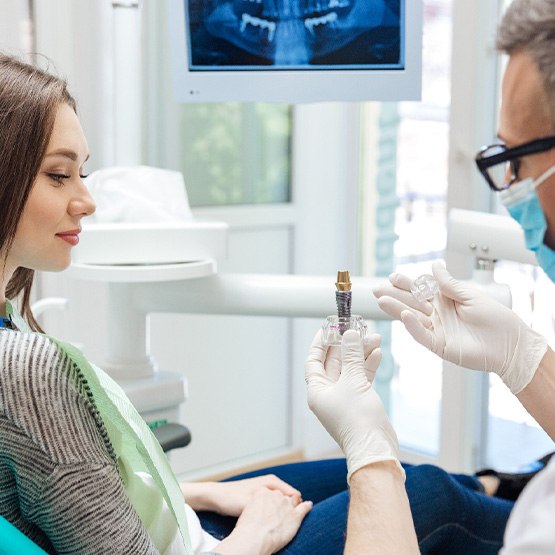 Dentist showing sample dental implant to woman in dental chair