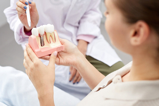 Dentist pointing to sample implant held by patient