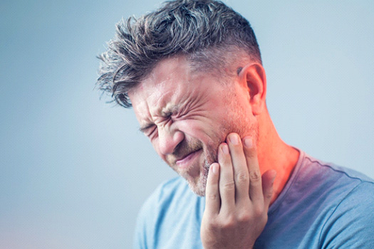 Man in blue shirt squinting eyes and touching jaw in pain