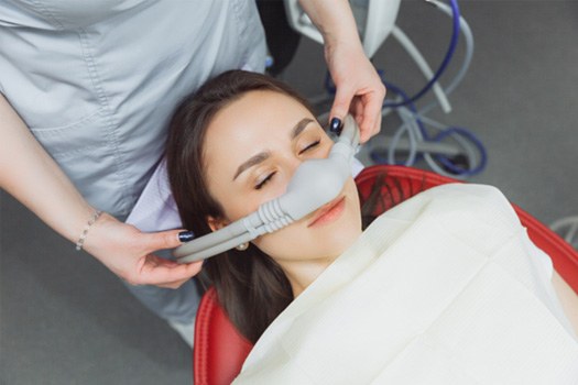Woman laying in dental chair with nitrous oxide mask over nose
