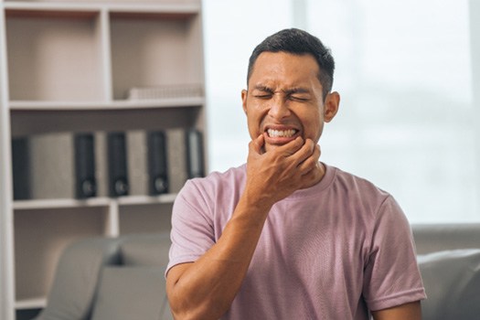 Man in pink shirt squinting and touching corners of mouth in pain