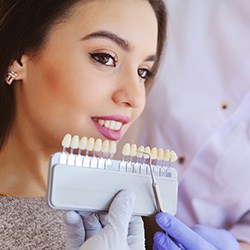 Woman in dental chair smiling with shade guide held to her teeth