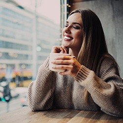 Woman holding coffee looking out café window smiling